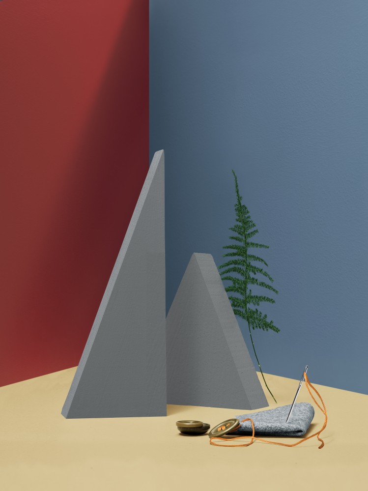 Duas pirâmides cinzentas em cima de uma mesa com dois botões dourados e uma agulha com linha laranja
